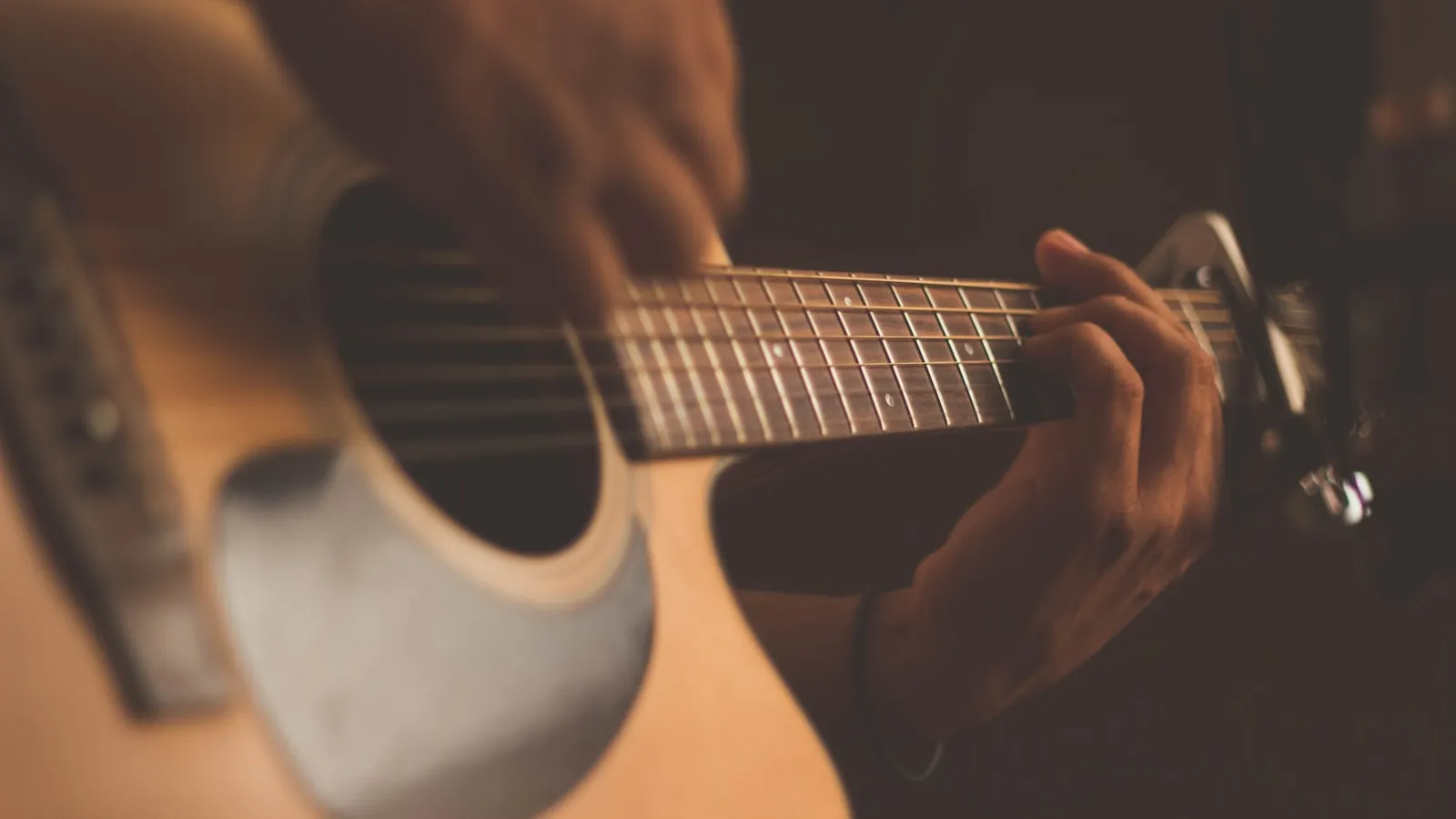 Close-up of a hand fretting chords on an acoustic guitar
