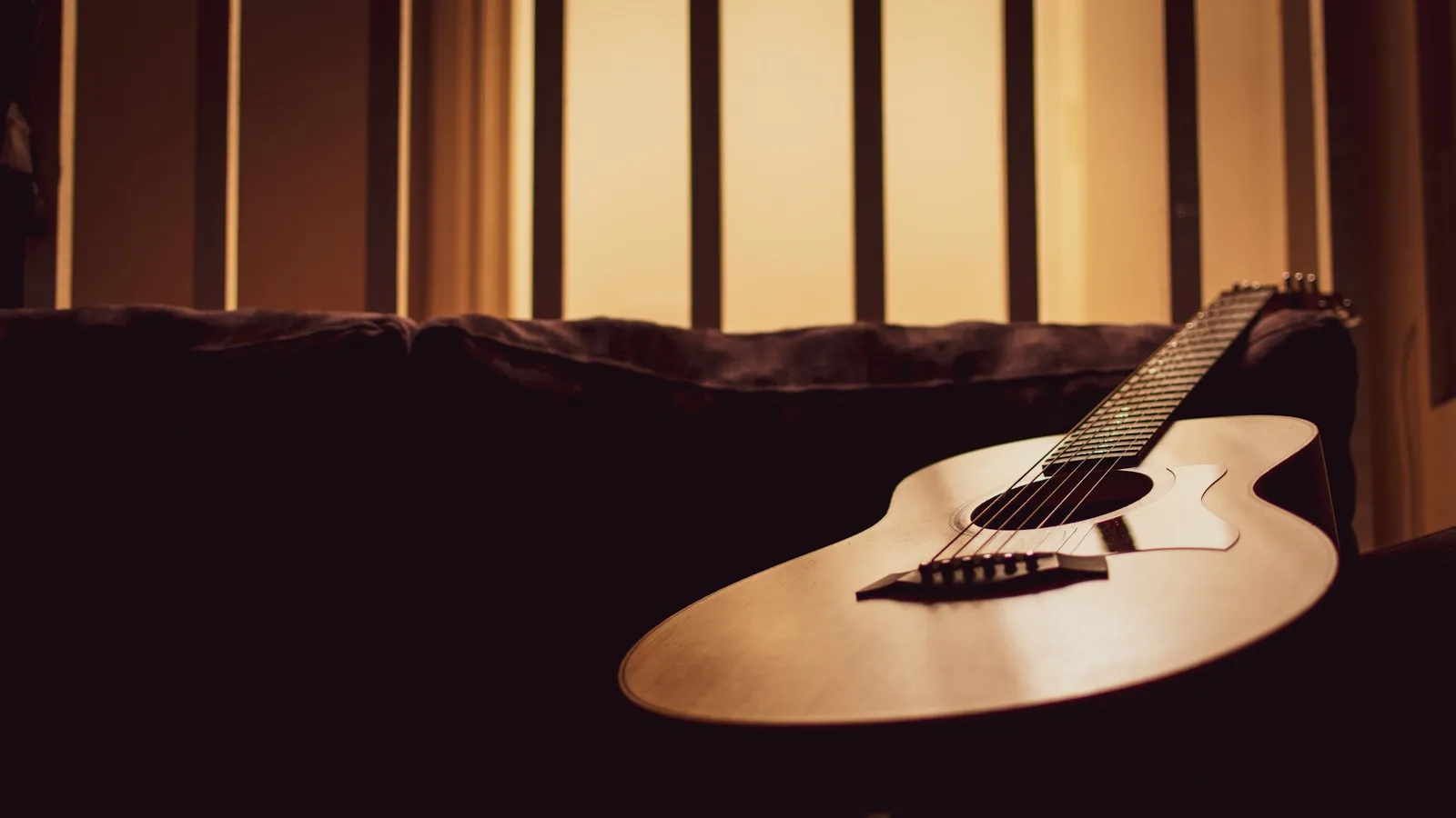 An acoustic guitar resting on a sofa in warm evening light
